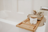 Luxurious bathroom setting featuring a bamboo bathtub caddy with cotton balls, books, and flowers for a serene spa-like experience.
