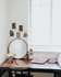 Charming study nook with a sleek wooden desk, decorative wall art, and a round mirror, illuminated by natural light from a window with white blinds.