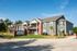 Charming apartment complex exterior with modern architecture, well-maintained green lawns, and a welcoming entrance under a clear blue sky.