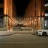 Charming evening view of a modern brick building entrance with stylish string lights and inviting outdoor seating.