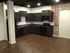 Modern kitchen with sleek dark cabinets, exposed brick accent wall, and warm wooden flooring, creating an inviting and stylish atmosphere.