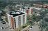 Aerial view of modern apartment buildings with sleek solar panels, nestled in a scenic neighborhood surrounded by lush greenery and suburban homes.