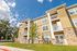 Modern three-story apartment building with stone accents, lush green surroundings, and clear blue skies.