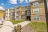 Charming three-story apartment complex with modern architectural details, lush lawn, and vibrant landscaping under a bright blue sky.