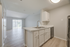 Bright, modern kitchen with sleek white cabinetry, expansive countertops, and an open-concept living area with stylish wood flooring leading to large windows.