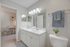 Bright and modern bathroom with double sinks, sleek mirror, and soft blue accents, leading to a cozy office nook.