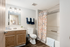 Bright, inviting bathroom featuring elegant lighting, chic shower curtain, and stylish wood cabinetry.