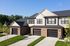 Charming townhouse duo with modern brick facade and sleek black garage doors, set in a lush green neighborhood.