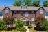 Charming brick townhouse with dormer windows, abundant natural light, surrounded by lush green trees.