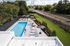 Chic apartment complex with a stylish outdoor pool, sun loungers, and umbrellas surrounded by lush greenery and open spaces.