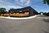 Modern industrial building featuring sleek black facade with decorative wooden accents and neatly landscaped greenery on a spacious lot.