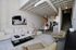 Modern open-concept living space featuring a sleek white sofa, stylish armchairs, and contemporary art. Spacious kitchen area with stainless steel appliances and elegant dining setup, enhanced by industrial-style ceiling beams.
