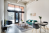Bright and modern living space with high ceilings, large windows, and chic turquoise sofa. Contemporary dining area and artistic decor enhance the inviting ambiance.