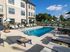 Luxurious apartment complex with a sparkling outdoor pool, surrounded by stylish lounge chairs and vibrant green umbrellas, perfect for relaxation and leisure.