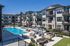 Luxurious apartment complex with modern three-story buildings surrounds a sparkling outdoor swimming pool, featuring cozy lounge areas and a stylish fire pit.