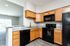 Modern kitchen with sleek black appliances, elegant wooden cabinetry, and spacious countertops, flowing into a bright living area with natural light.