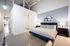 Modern bedroom with elegant blue bed, stylish bedside lamps, and an en-suite bathroom in a chic loft apartment.
