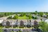 Aerial view of a charming residential neighborhood featuring picturesque townhouses, lush greenery, and ample parking space under a clear blue sky.