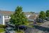 Charming suburban neighborhood featuring duplex homes with well-maintained lawns, ample parking, and lush greenery under a clear blue sky.