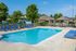 Inviting apartment complex pool with vibrant blue lounge chairs and a nearby playground, offering a perfect family-friendly leisure setting.
