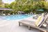 Inviting outdoor pool area with stylish lounge chairs, surrounded by lush greenery and shaded seating, perfect for relaxation and leisure.