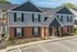 Charming multi-unit apartment building with brick accents, surrounded by lush greenery and featuring a welcoming outdoor patio.