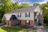 Charming two-story home with a brick facade and cozy balcony surrounded by lush greenery, perfect for serene living.