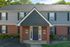 Charming two-story brick apartment building entrance with elegant landscaping and lush greenery, showcasing a welcoming and stylish exterior.