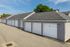 Modern apartment complex garages with sleek gray siding and white doors, ample parking, and lush green surroundings.