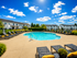 Inviting outdoor pool area with sun loungers, surrounded by well-maintained landscaping and charming townhouse views under a bright blue sky.