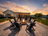 Charming outdoor patio featuring a cozy fire pit surrounded by Adirondack chairs, with a picturesque pergola and beautiful sunset backdrop.
