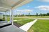 Inviting front porch with landscaped gardens overlooking a scenic green expanse and a quiet street, perfect for relaxation.