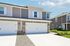 Modern townhouse exterior with a double garage, sleek siding, and stone accents, set in a sunny and vibrant neighborhood.