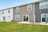 Charming townhouse with modern siding, lush green lawn, large windows, and inviting patio doors for a bright living experience.