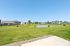 Charming neighborhood scene with lush green lawns, modern homes, and a serene pond under a clear blue sky.