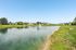 Scenic view of tranquil pond with fountain surrounded by lush lawns and charming residential homes under a clear blue sky.