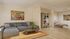 Elegant living room showcasing a cozy gray sectional sofa, stylish coffee table, and a vibrant painting, adjacent to a serene bedroom with modern decor.
