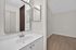 Modern bathroom with sleek white vanity, elegant sink, and large mirror reflecting wood-style flooring.