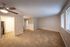 Spacious living area with warm carpeting and ample natural light, featuring a modern ceiling fan and a glimpse into the sleek kitchen.