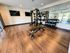 Modern fitness center with sleek wooden flooring, featuring a versatile power rack, weight bench, and neatly organized dumbbell set under warm lighting.