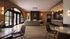 John Ourdue Luxurious open-concept lounge with elegant brick walls, modern fireplace, and ample natural light from large arched windows.