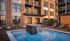 Elegant urban courtyard with brick facade, stylish balconies, and a serene poolside oasis featuring comfortable loungers.