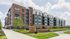 Modern apartment complex with a sleek brick and panel facade, surrounded by landscaped greenery and wide pathways.