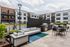 Chic outdoor community space with modern seating, BBQ grills, and a vibrant pool area surrounded by contemporary apartment buildings, perfect for relaxation and social gatherings.