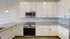 Modern kitchen featuring sleek white cabinetry, stainless steel appliances, and elegant gray backsplash.