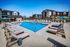 Luxury apartment community featuring a pristine swimming pool surrounded by stylish lounge chairs and umbrellas, perfect for sunny relaxation and leisure.