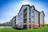 Elegant, modern apartment building with large windows, balconies, and attractive brick and panel siding, surrounded by lush greenery.