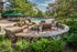 Charming outdoor seating area with a cozy fire pit overlooking a luxurious pool, surrounded by lush greenery and stylish lounge chairs.