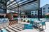 Modern apartment complex featuring a stylish outdoor patio with stainless steel grills, vibrant turquoise seating, and a sparkling swimming pool under a sunny sky.
