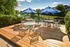 Charming outdoor patio with wooden decking, featuring colorful seating and blue umbrellas, overlooking a serene pond.